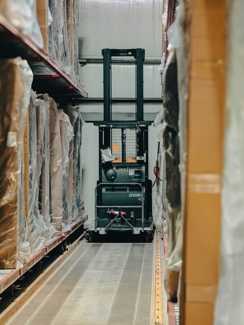 Reach truck lifting palletised goods between high racking